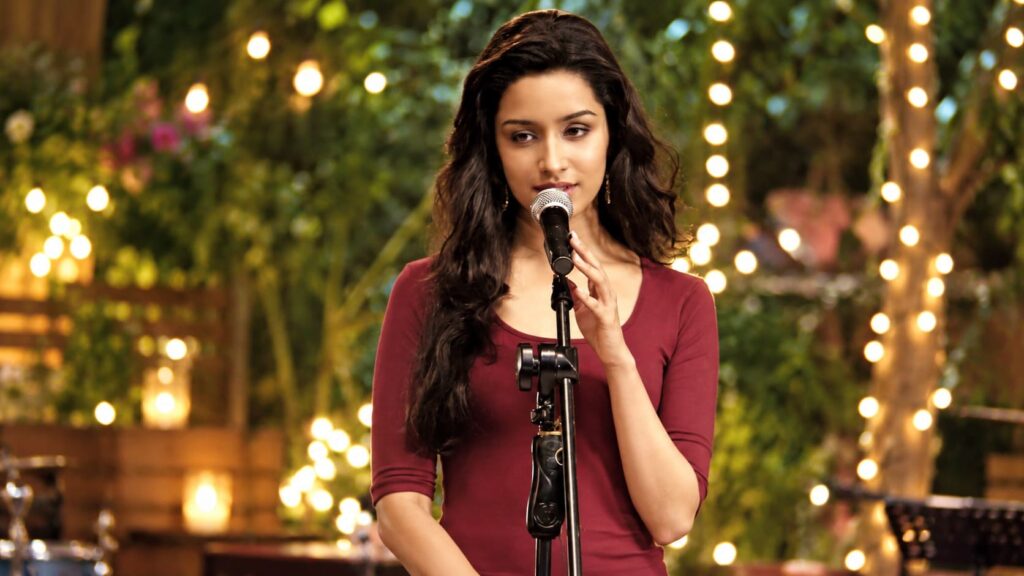 Aarohi singing into a microphone against warm lights and greenery, inspired by Aashiqui 2.